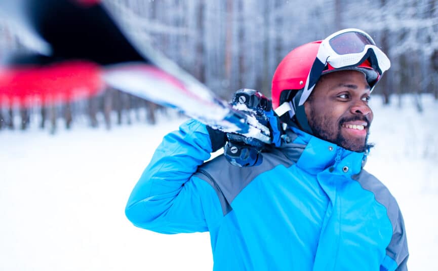 A man in ski outfit carrying his skis on his shoulder