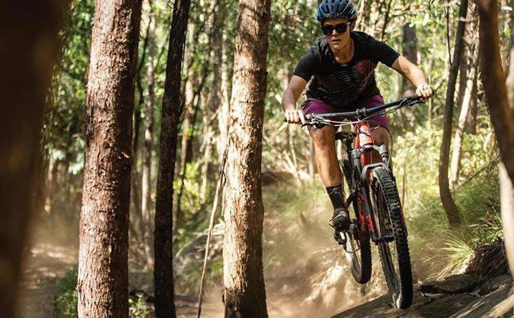 a lady riding a mountain bike through the trails with a helmet and sunglasses on
