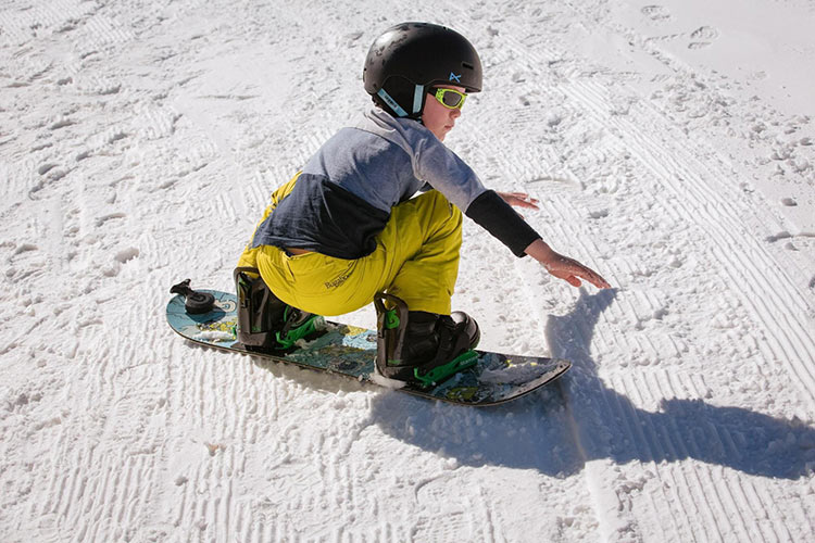 a kid crouching down on the ground ready to turn on their snowboard